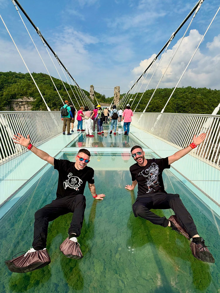 Christopher and Jesse from Borderless Bros Club strike a joyful pose on the iconic Zhangjiajie Glass Bridge in China, capturing their fearless and playful travel style.